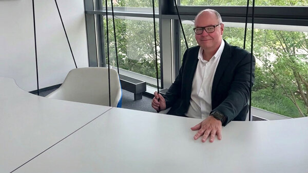 Kai Kröger zum Thema „Alte Taxdoo-Verrechnungskonten in der Buchhaltung“. Er sitzt in modernem Büro vor  großen Fenstern mit Blick auf den Lenkwerk Campus Bielefeld.